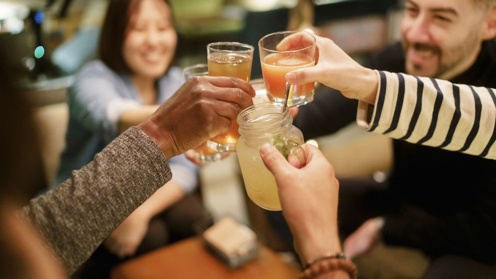 A multi-ethnic group of friends are enjoying toasting with cocktails and beer in a cafe.