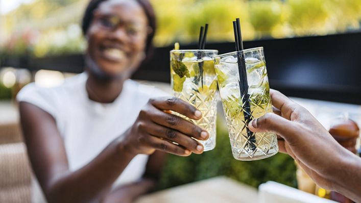 Beautiful young black couple drinking mojito cocktails in a bar outdoors. Having a celebratory toast.